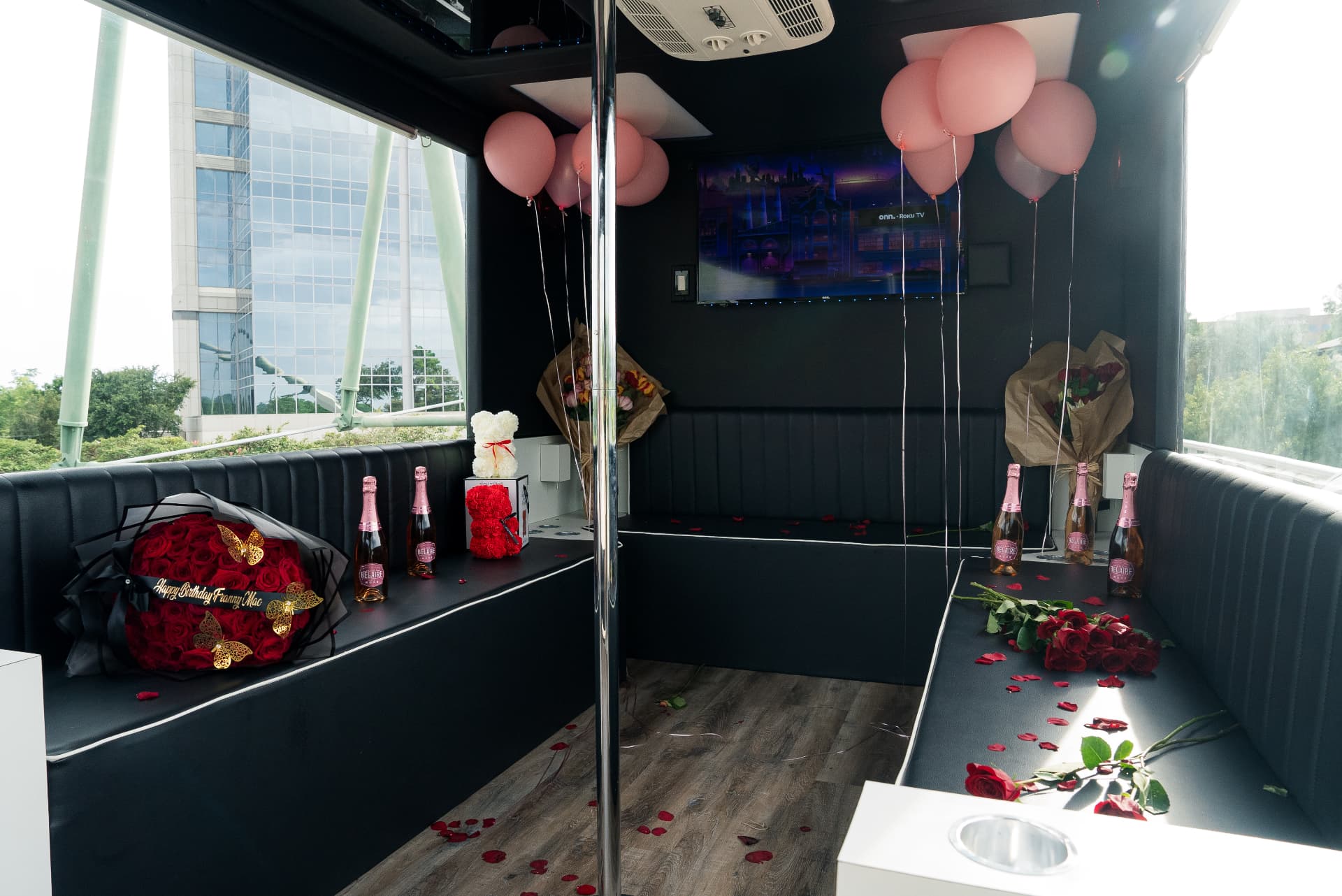 Glass bus interior fully decorated with balloons, rose bouquets, a rose bear, bottles of rosé and petals across the seats