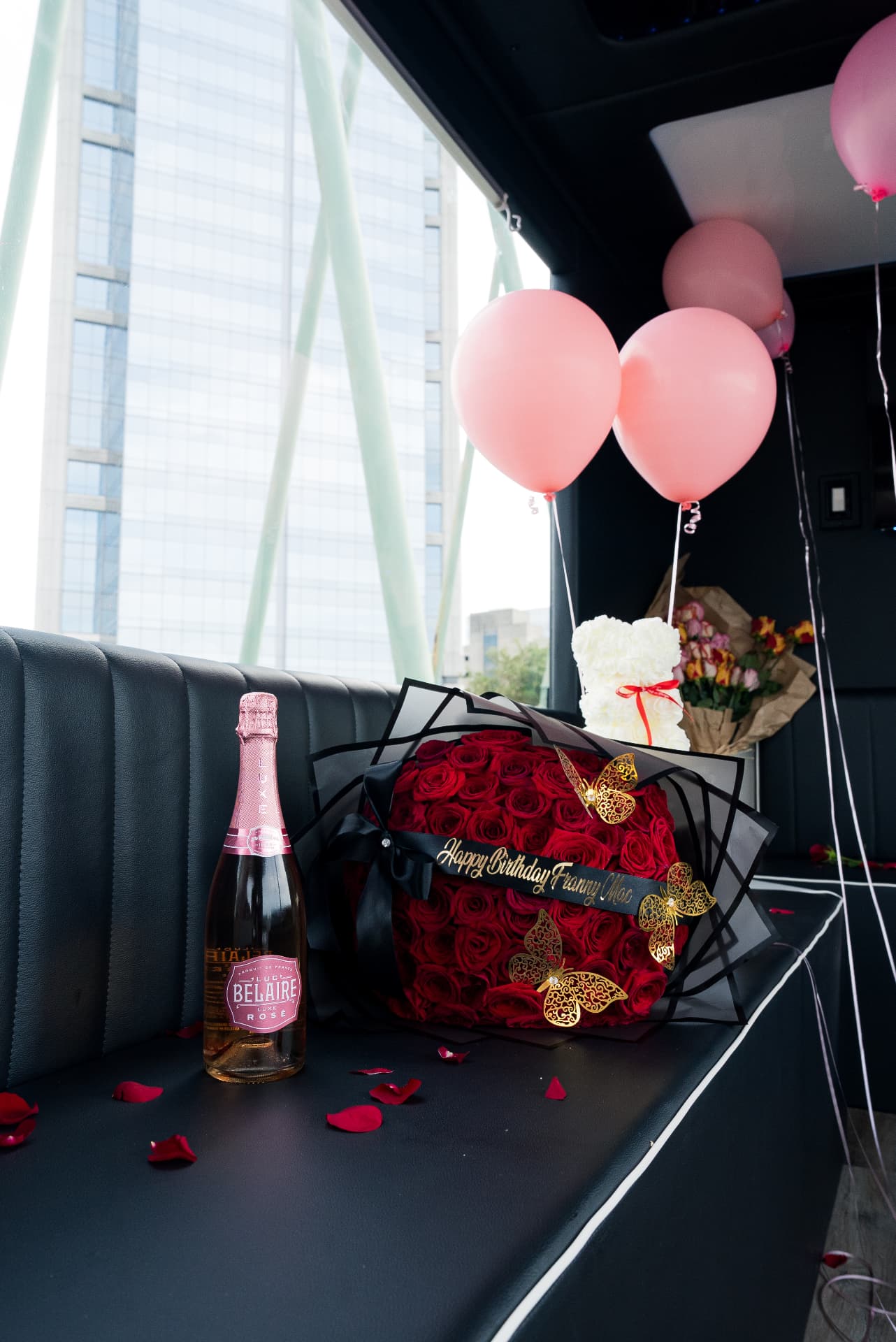 Wrapped bouquet of red roses with a Happy Birthday ribbon, gold butterflies, rosé and pink balloons on board